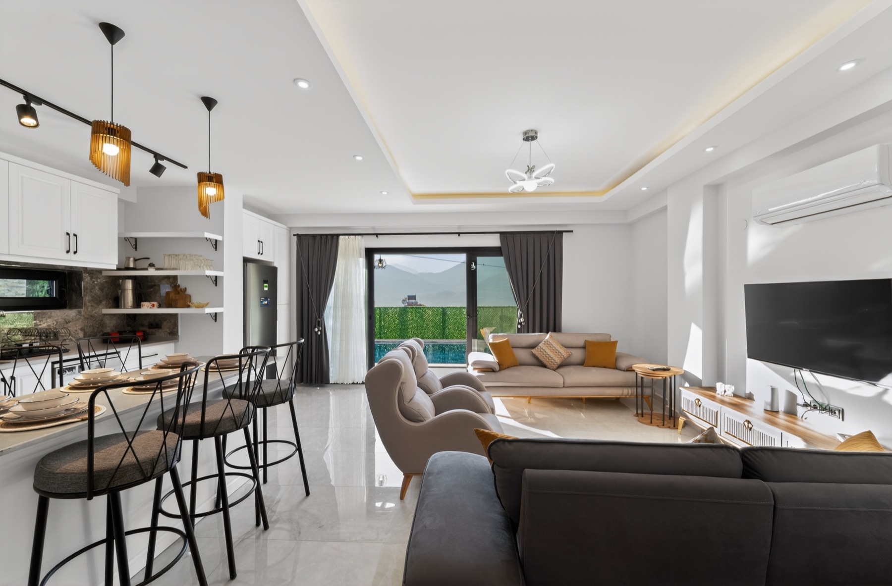 Açık plan salon ve mutfak; ada, bar taburesi ve bahçeye açılan cam cephe.