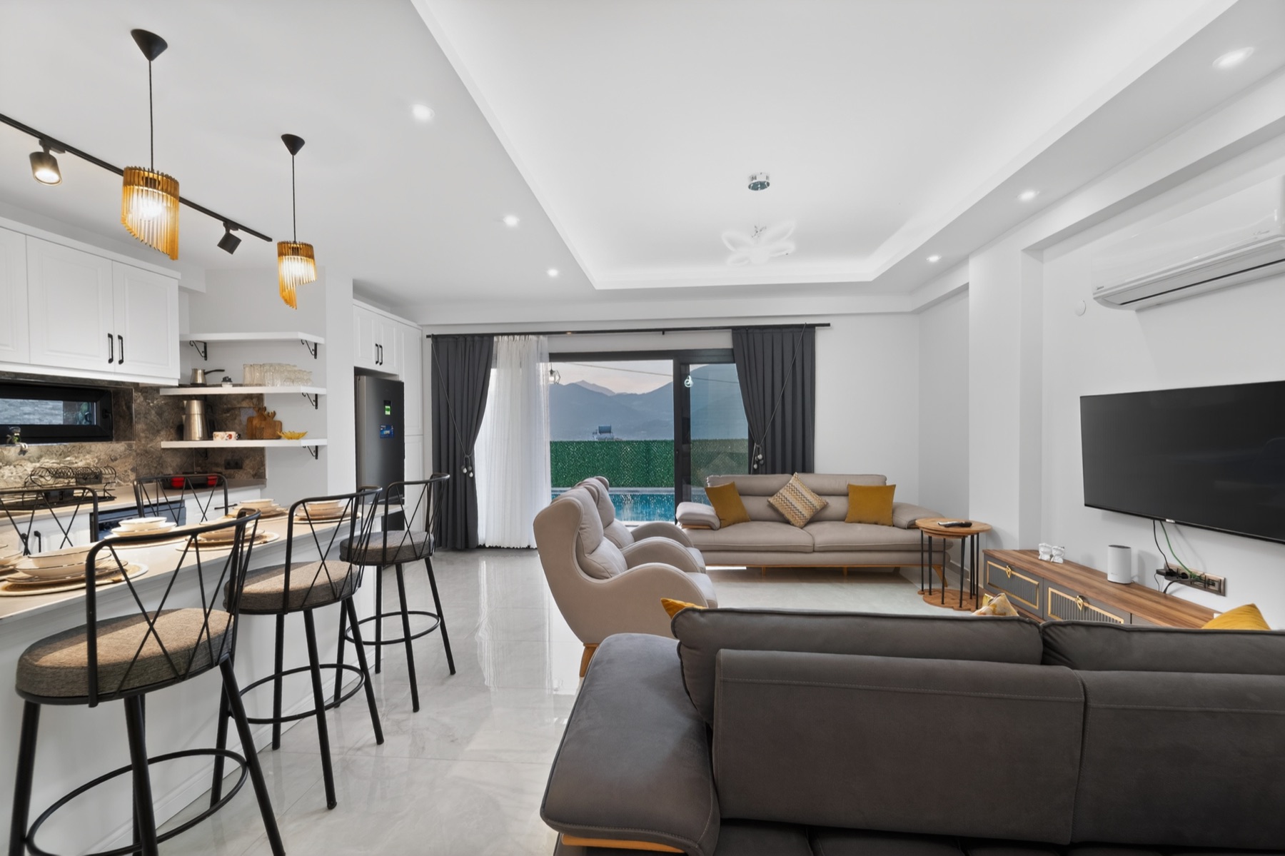 Salon ve mutfak arası bar taburesi; cam cepheden bahçe.