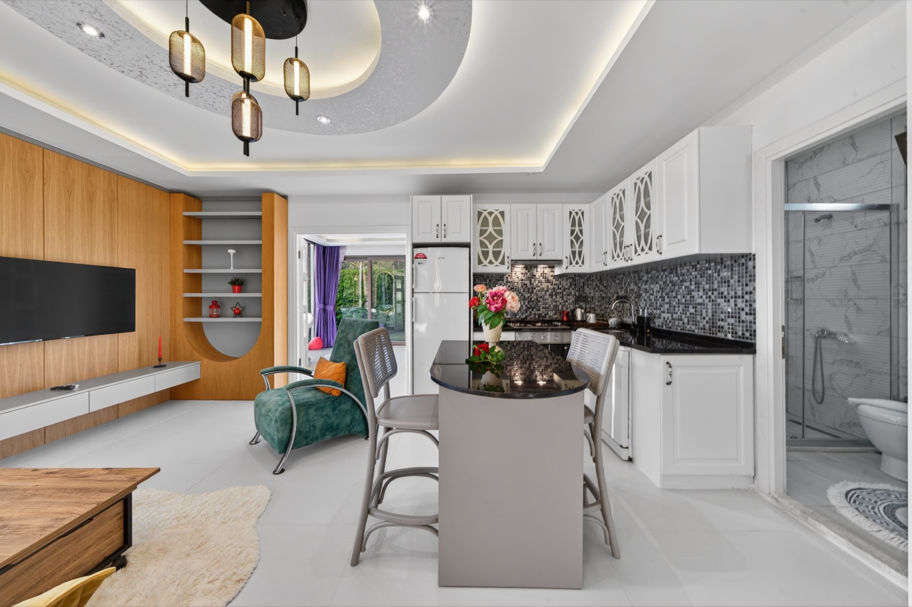 Açık plan salon ve mutfak; avize ve ahşap kaplı duvar.